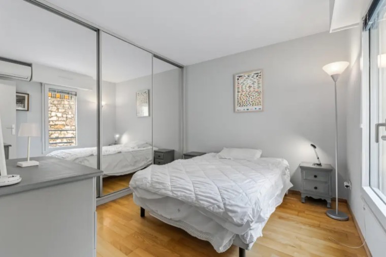 Bedroom with an unmade bed, reflected in a wall of mirrored wardrobe doors